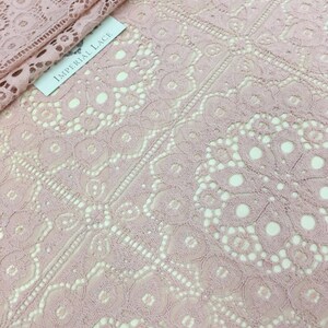 May include: Pale pink lace fabric with a delicate floral pattern. The fabric has a soft, airy feel and is perfect for creating garments, accessories, or home decor.