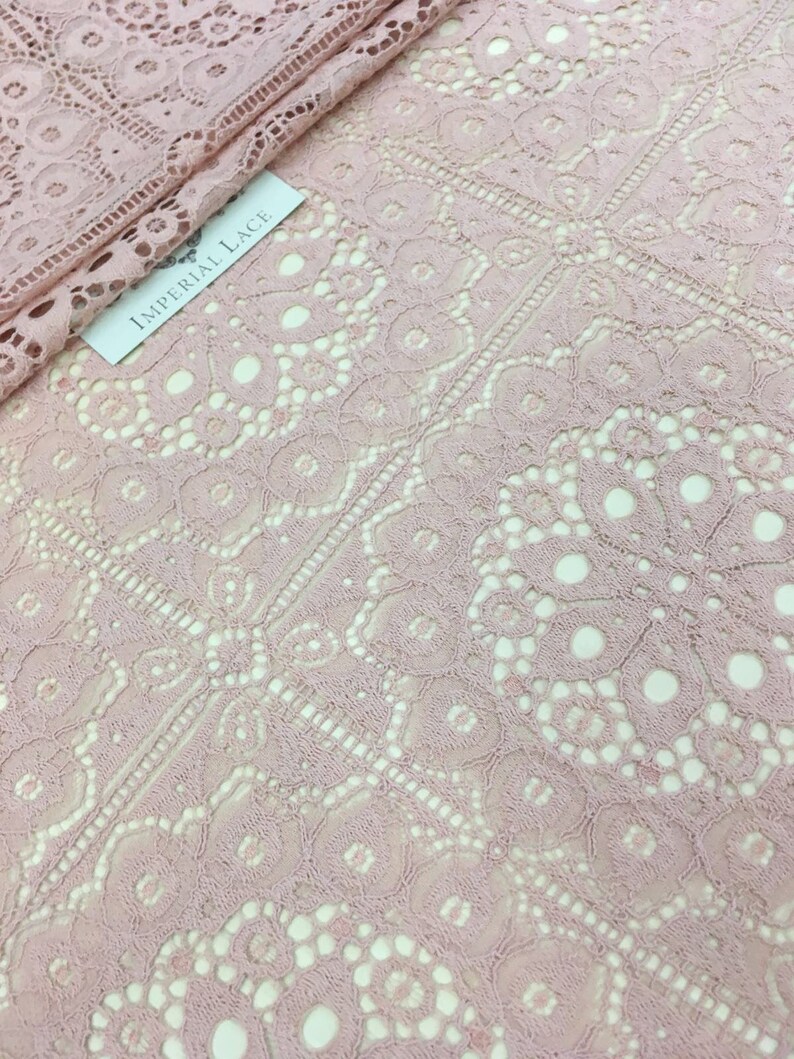 May include: Pale pink lace fabric with a delicate floral pattern. The fabric has a soft, airy feel and is perfect for creating garments, accessories, or home decor.
