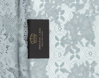 May include: A close-up of light blue lace fabric with a floral pattern. The fabric is folded in half and a black tag with the text "IMPERIAL LACE French lace dealer" is visible.