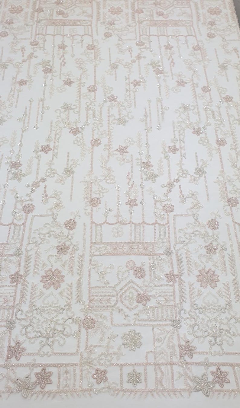 May include: White beaded fabric featuring a delicate floral pattern and geometric shapes. The fabric has a subtle shimmer and is ideal for adding a touch of elegance to any project.