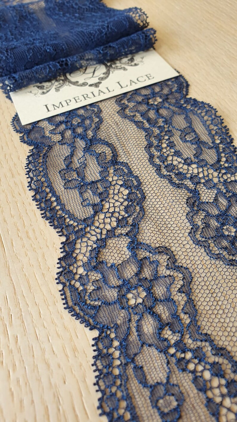 May include: Navy blue lace trim with a delicate floral pattern. The lace is shown on a wooden surface with a tag that reads "Imperial Lace".
