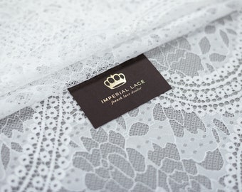 Puede incluir: Tela de encaje blanca con un delicado patrón floral. Una tarjeta marrón con letras doradas dice "Imperial Lace, French lace dealer".