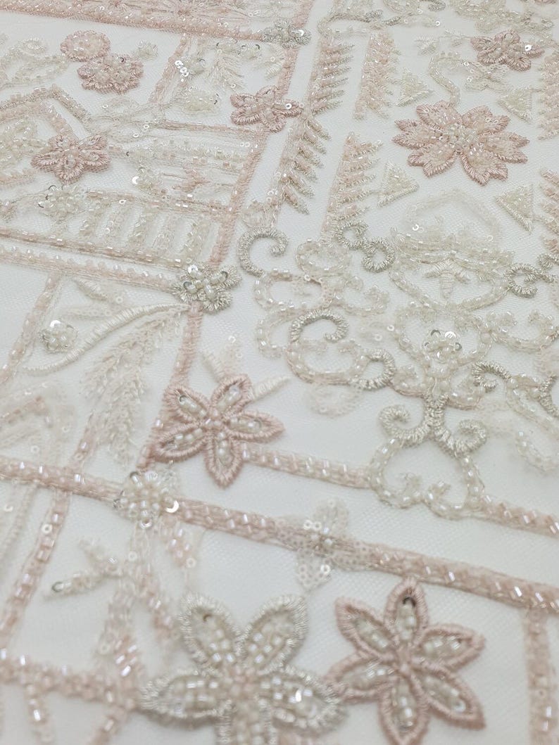May include: White and pink beaded fabric with a geometric pattern. The fabric is made of a sheer mesh material and is decorated with small beads and sequins.