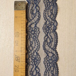 May include: A close-up of navy blue lace trim with a floral pattern. The lace is measured against a wooden ruler with markings in inches and centimeters. The label reads "Imperial Lace".