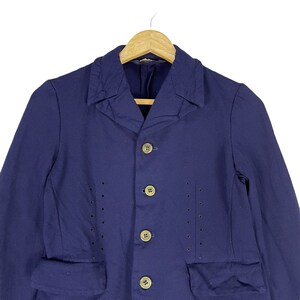 Puede incluir: Una chaqueta azul marino con cuello y cinco botones. La chaqueta tiene dos bolsillos de solapa y un patr&oacute;n decorativo de peque&ntilde;os agujeros en la parte delantera.