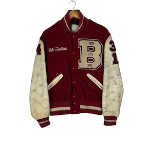 May include: A vintage maroon and cream varsity jacket with the name "Rob Truskett" embroidered on the chest. The jacket features a large "B" patch and the number "31" on the sleeves. The sleeves are cream-colored.
