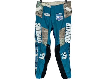 May include: Blue and white motocross trousers with the word "SINISALO" printed on the sides. The trousers have a black panel on the knees and a white patch on the right thigh with the word "SINISALO" printed on it.