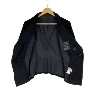 May include: A black double-breasted wool coat with a Y's for Yohji Yamamoto label on the inside. The coat is hanging on a wooden hanger.