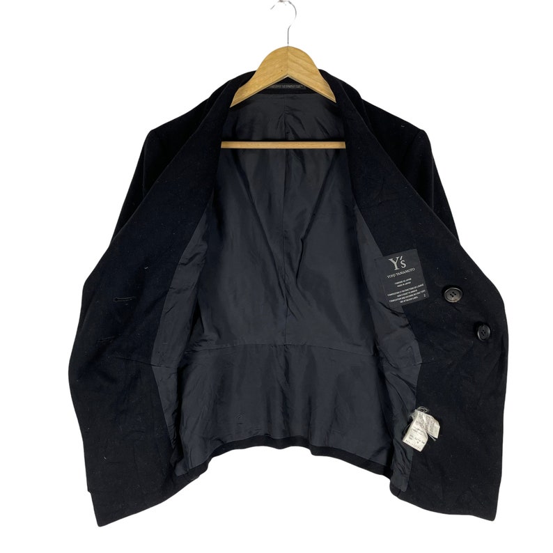 May include: A black double-breasted wool coat with a Y's for Yohji Yamamoto label on the inside. The coat is hanging on a wooden hanger.