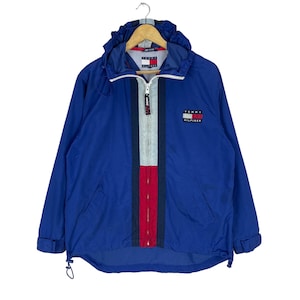 Puede incluir: Una chaqueta azul con capucha y una franja roja, blanca y azul en la parte delantera. La chaqueta tiene un logotipo de Tommy Hilfiger en el pecho.
