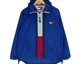 May include: A blue hooded jacket with a red, white, and blue stripe down the front. The jacket has a Tommy Hilfiger logo on the chest.