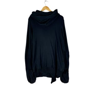 May include: Black hooded sweatshirt with a long, flowing design. The sweatshirt has a large hood and a relaxed fit.