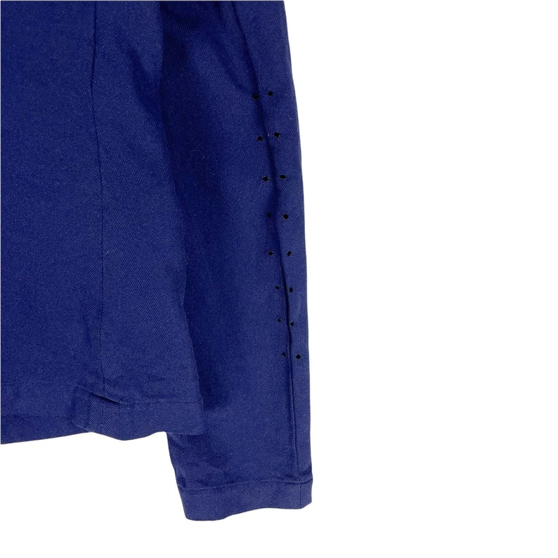 Puede incluir: Una camisa de manga larga azul marino con una fila de peque&ntilde;os agujeros en la manga derecha.