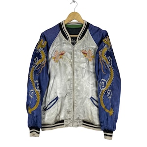 May include: A silver satin bomber jacket with blue satin sleeves. The sleeves feature embroidered gold dragons. The jacket has a zipper closure and a ribbed collar, cuffs, and waistband.