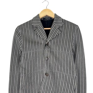 Op de afbeelding: Een grijs en zwart gestreepte blazer met drie knopen, hangend aan een houten hanger. De blazer heeft een revers en de tekst "i wish" is zichtbaar op het label.