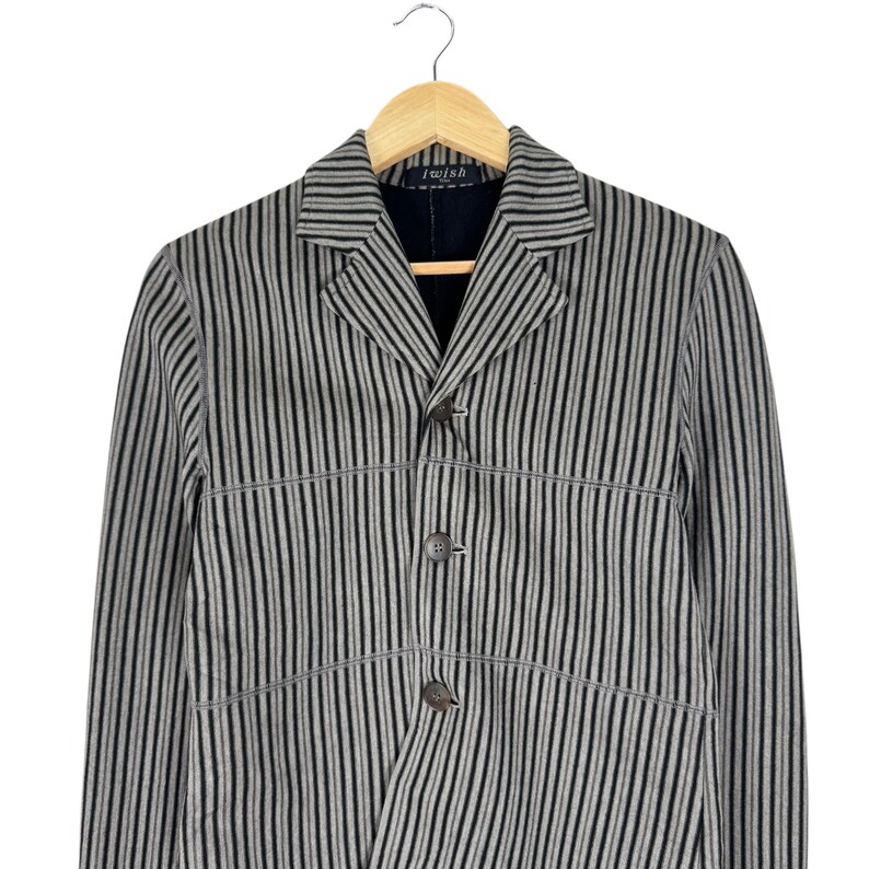 Op de afbeelding: Een grijs en zwart gestreepte blazer met drie knopen, hangend aan een houten hanger. De blazer heeft een revers en de tekst "i wish" is zichtbaar op het label.