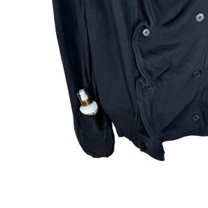 May include: A black double-breasted cardigan with a pocket on the left sleeve. A small bottle of lotion is in the pocket.