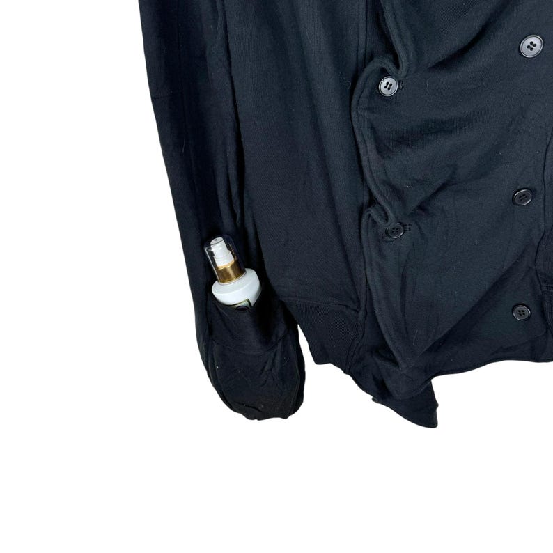 May include: A black double-breasted cardigan with a pocket on the left sleeve. A small bottle of lotion is in the pocket.