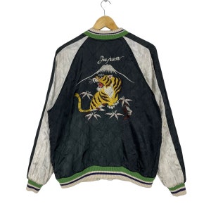 May include: Black satin bomber jacket with a white tiger embroidered on the back. The tiger is surrounded by bamboo and a mountain with the word "Japan" above it. The jacket has green and white striped ribbing at the collar, cuffs, and hem.