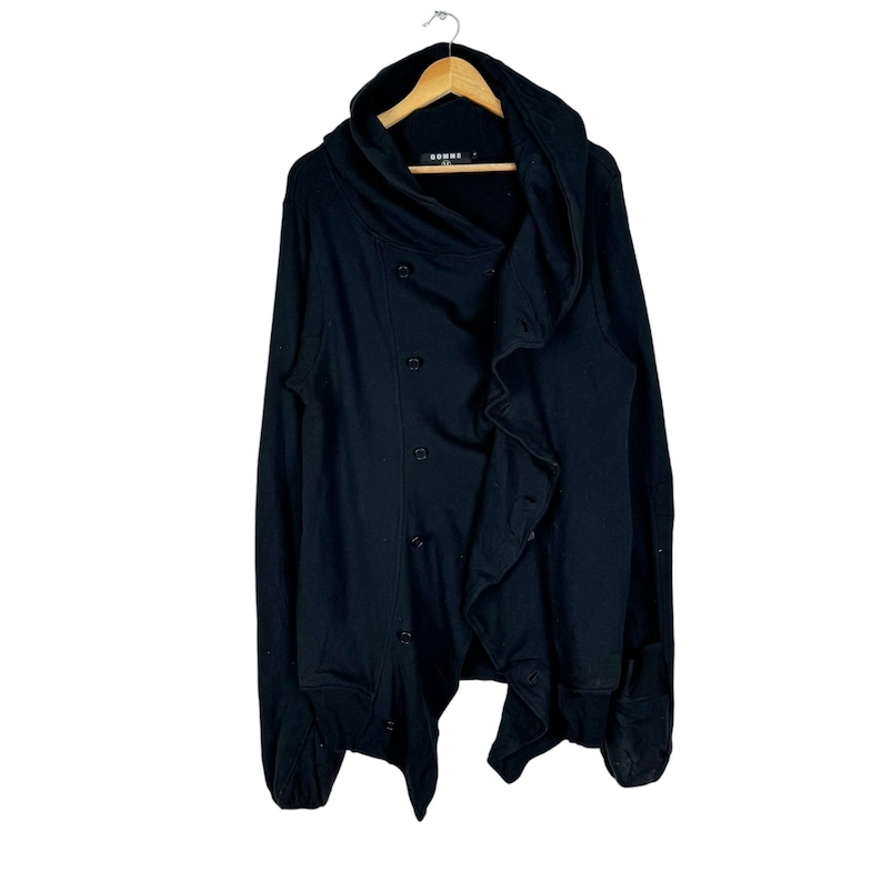 May include: Black hooded cardigan with a draped, asymmetrical design and button closures. The cardigan has a long, flowing silhouette and a relaxed fit.