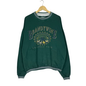 May include: Green sweatshirt with a white and navy blue striped collar and cuffs. The front of the sweatshirt features a gold embroidered logo that says "Brandywine Traditional Golf Country Club".