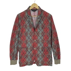 May include: A red, grey, and brown argyle patterned blazer with three buttons and two front pockets. The blazer is hanging on a wooden hanger. The cuffs are a solid brown colour.
