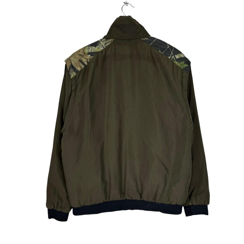 May include: A dark green jacket with a camouflage pattern on the shoulders and a black ribbed waistband.