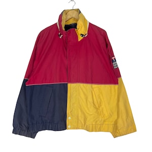 Puede incluir: Una chaqueta de color rojo, azul y amarillo con cierre de cremallera y un logotipo que dice "Sail Gear" en la manga derecha.