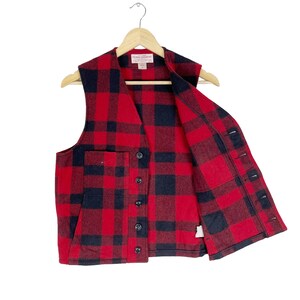 Op de afbeelding: Rood en zwart geruit flanellen vest met een knoopsluiting en twee zakken. Het vest is gemaakt door Filson Garment Co.