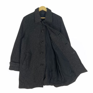 May include: A gray tweed overcoat with a black lining and button closure. The coat has a classic style and is perfect for colder weather.