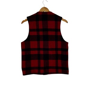 Puede incluir: Un chaleco a cuadros rojos y negros colgado de una percha de madera. El chaleco tiene un estilo cl&aacute;sico de le&ntilde;ador con una parte delantera abotonada y cuello en V. La tela parece ser lana gruesa o una mezcla de lana.