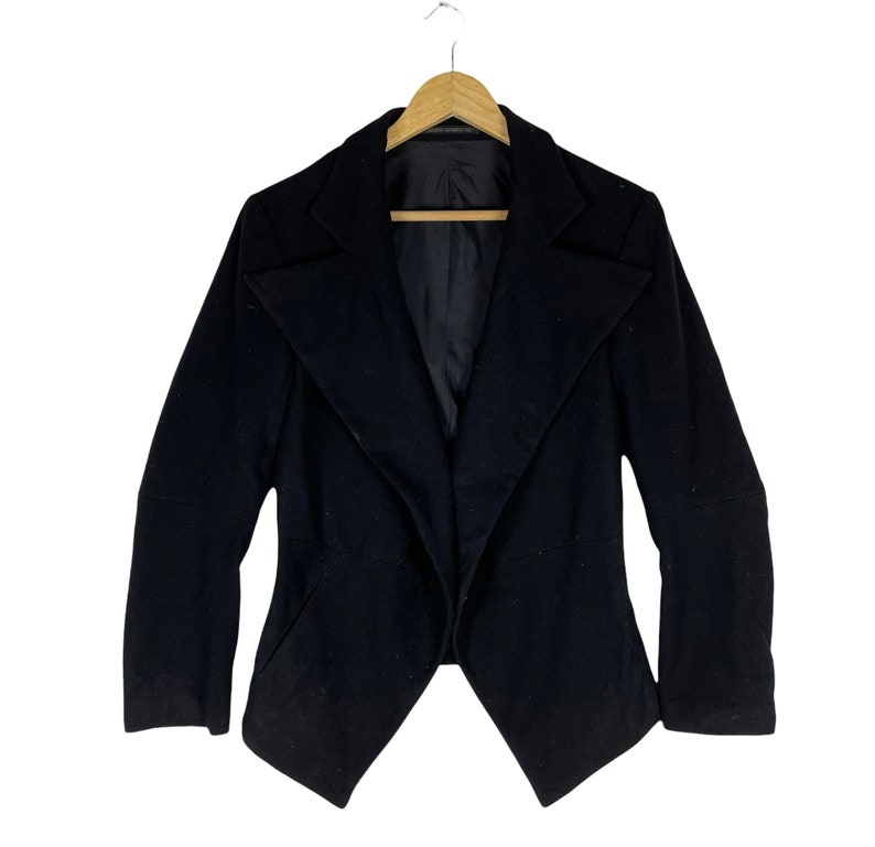 May include: A black blazer with a long, pointed collar and a draped front. The blazer has long sleeves and a fitted silhouette.
