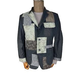 May include: A black patchwork jacket featuring a variety of patterned fabric panels. The jacket has a button-up front, two flap pockets, and a collar.