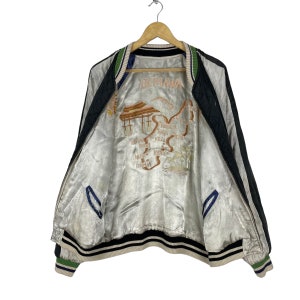 May include: A black and white reversible bomber jacket with a satin lining. The lining features an embroidered map of Okinawa, Japan with the text "Okinawa" in the center.