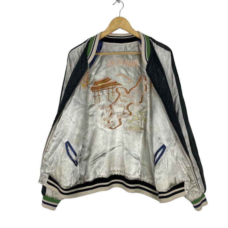 May include: A black and white reversible bomber jacket with a satin lining. The lining features an embroidered map of Okinawa, Japan with the text "Okinawa" in the center.