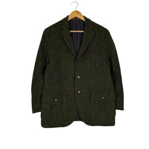 May include: A dark green blazer with a textured fabric, hanging on a wooden hanger. The blazer has four front pockets, a notched lapel, and a three-button closure. The interior lining is striped.