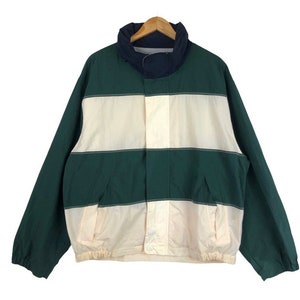 Puede incluir: Una chaqueta a rayas de color blanco y verde. La chaqueta tiene un cuello azul marino y una cremallera.