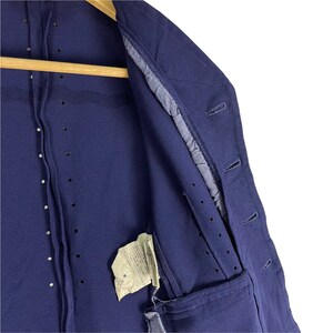 Puede incluir: Una chaqueta azul marino con cierre de botones y un solo bolsillo en el lado izquierdo. La chaqueta tiene un interior forrado y una etiqueta con texto japon&eacute;s.