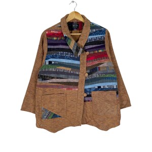 May include: A brown jacket with a patchwork design on the front. The patchwork is made of different colored fabrics, including blue, green, red, and yellow. The jacket has a collar and two pockets.