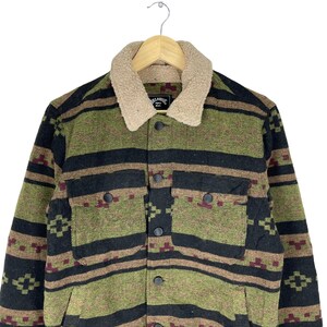 May include: A green, black and brown patterned jacket with a sherpa collar. The jacket has a button closure and two flap pockets. The label on the jacket reads "Billabong 22".