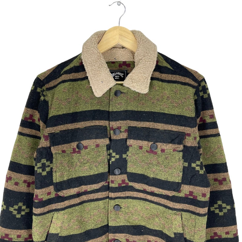 May include: A green, black and brown patterned jacket with a sherpa collar. The jacket has a button closure and two flap pockets. The label on the jacket reads "Billabong 22".