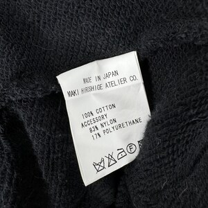 May include: White care label with black text that reads "MADE IN JAPAN MAKI HIROSHIGE ATELIER CO. 100% COTTON ACCESSORY 83% NYLON 17% POLYURETHANE". The label also has a black and white care symbol.