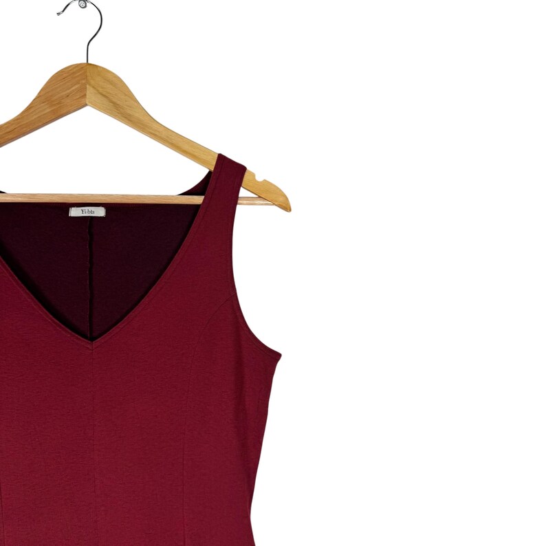Op de afbeelding: Een mouwloze, bordeauxrode jurk met een V-hals, hangend aan een houten kleerhanger. De jurk heeft een eenvoudig, elegant ontwerp, geschikt voor diverse gelegenheden. De hanger heeft de merknaam "Yible" erop.
