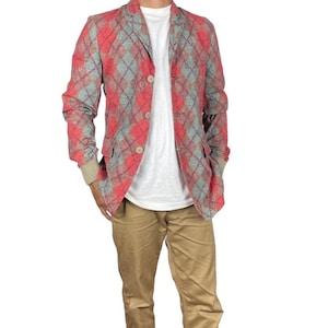 May include: A red, grey, and blue argyle patterned blazer with three beige buttons. The blazer has two front pockets and a beige cuff. The blazer is worn over a white t-shirt and paired with khaki trousers.