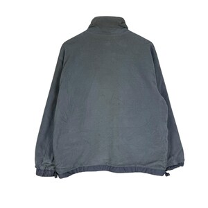 Puede incluir: Chaqueta polar gris oscuro con cuello alto y cremallera completa. La chaqueta tiene mangas largas y un cord&oacute;n en el dobladillo inferior. La tela parece suave y texturizada, adecuada para climas m&aacute;s fr&iacute;os.