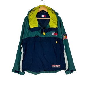 May include: A green, blue, and yellow hooded jacket with a Tommy Hilfiger logo on the front. The jacket has a zipper closure and a drawstring hood.