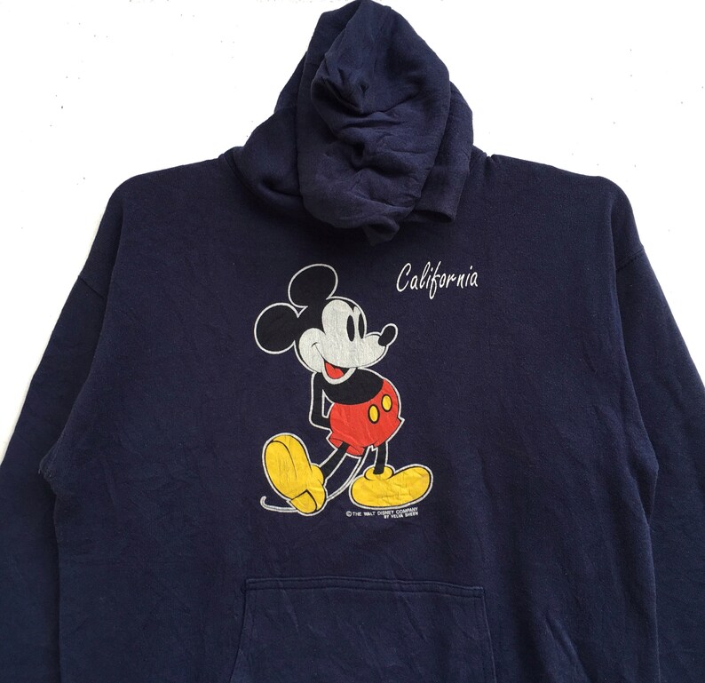 K&ouml;nnte beinhalten: Ein marineblauer Kapuzenpullover mit einem Mickey-Mouse-Motiv und dem Schriftzug "California" auf der Vorderseite.