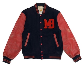 Op de afbeelding: Een marineblauwe varsity-jas met rode leren mouwen. De jas heeft rode knopen, een rood-marine gestreepte kraag en manchetten en een rood "MB"-patch op de borst. De jas heeft een vintage, versleten uitstraling.