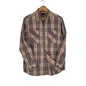 May include: A long-sleeved, button-down shirt with a plaid pattern in shades of gray, brown, and beige. The shirt has two chest pockets and is hanging on a wooden hanger. The shirt is made of a soft, comfortable material.