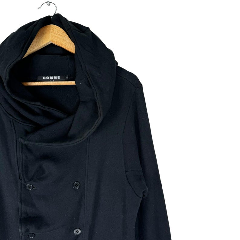 May include: Black hooded jacket with a double-breasted button closure and a large, draped collar. The jacket has the word "GOMME" printed on the label.